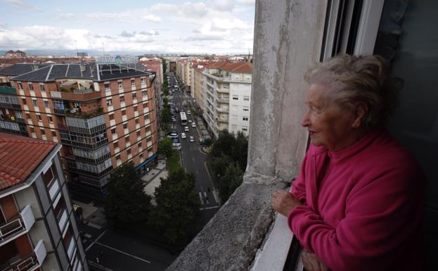 Una mujer observa el barrio desde su ventana.